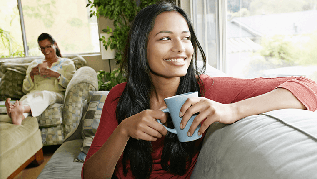A woman sitting by a window with tea and smiling